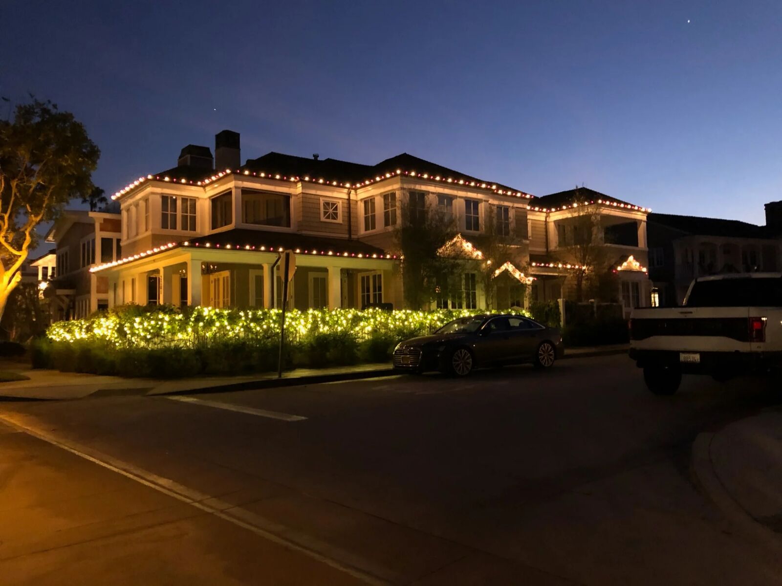 Two-story home with warm white roofline and lit hedges